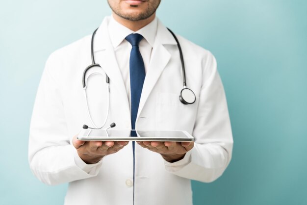 Midsection of male practitioner holding digital tablet while standing against blue background