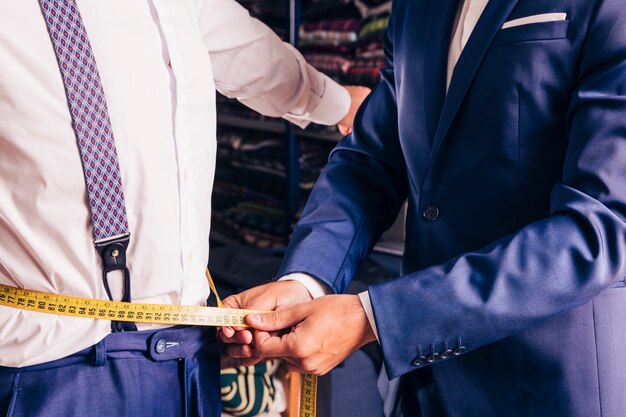 Midsection of a male tailor taking measurement of man's waist