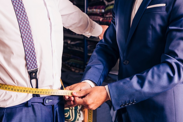 Midsection of a male tailor taking measurement of man's waist