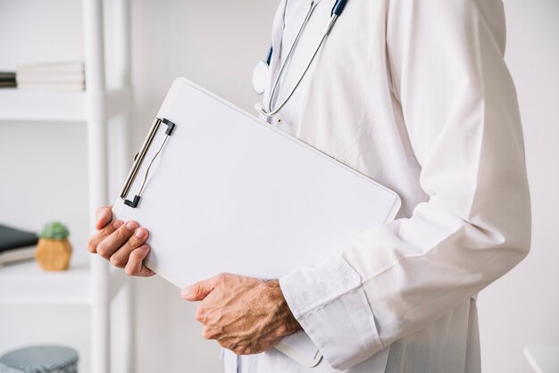 Вид средней части рук врача, держащего буфер обмена с пустой белой бумагой