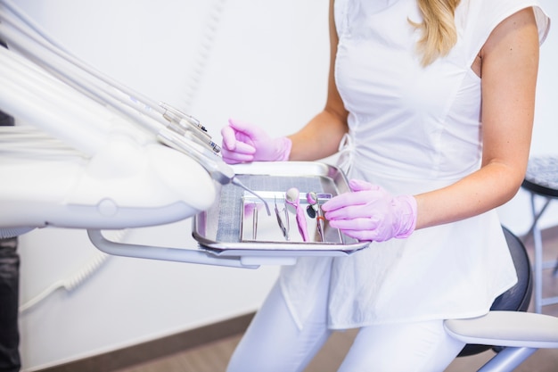 Midsection view of a female dentist with dental tools on tray