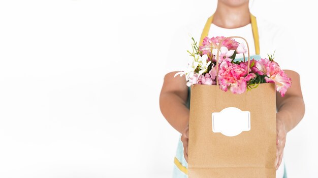 Midsection view of a florist hand holding paper bag full of flowers on white background