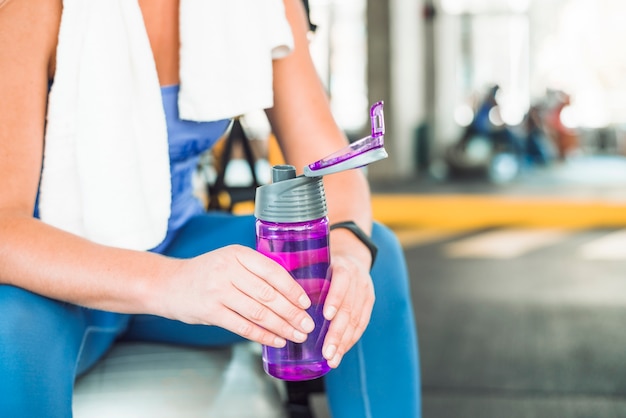 Midsection view of a woman's hand holding water bottle in gym