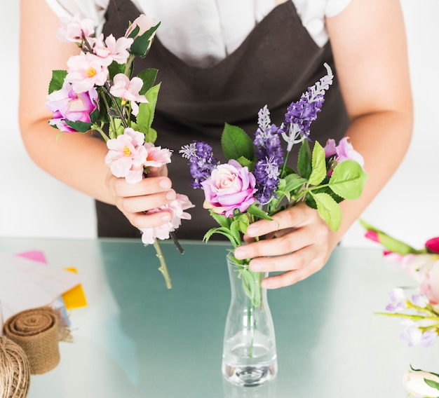 ガラスの机の花瓶に花を置く女性の手の中央部のビュー