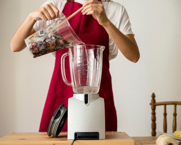 Midsection view of a woman's hand putting pieces of paper in blender