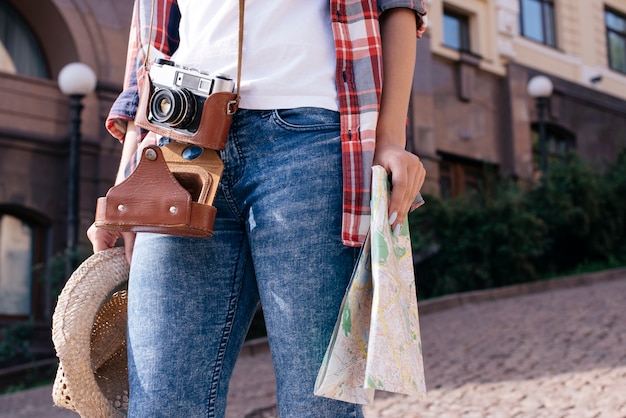 一人で旅行しながらカメラを運ぶと地図と帽子を保持している女性の中央部