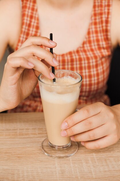 Midsection of woman sitting in caf� holding latte coffee cup and straw