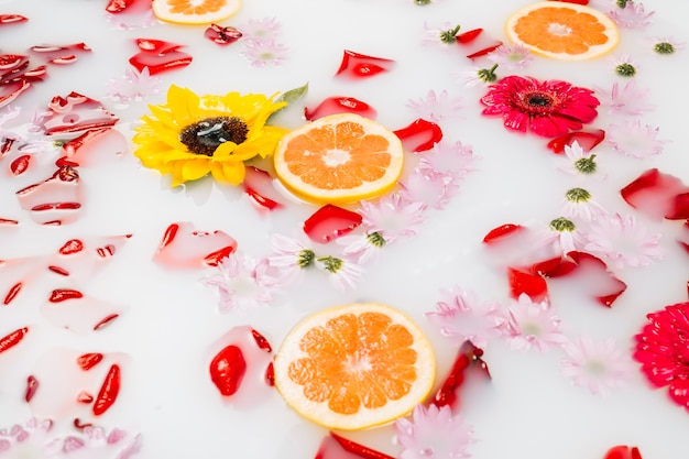 Milk bath decorated with various flowers, petals and slices of grapefruit