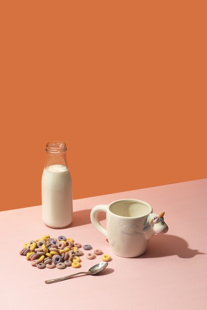 Milk bottle, colorful cereals and a glass with a unicorn on a pink surface