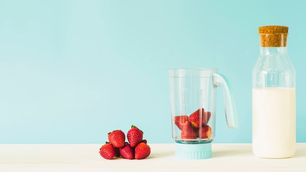 Milk bottle near strawberry in blender on wooden table