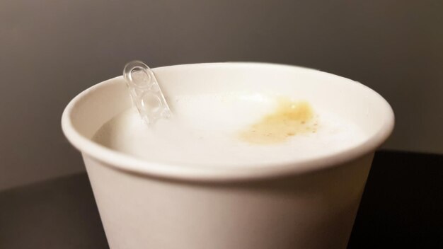 プラスチックスプーンスターラー​の​クローズアップ​と​自動​販売機​の​コーヒー​マシン​から​の​紙​の​白い​ガラス​の​ミルク​コーヒー​。