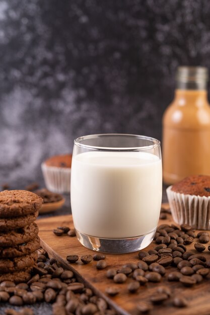 Молоко в стакане, в комплекте с кофе в зернах, кексы, бананы и печенье на деревянной тарелке.