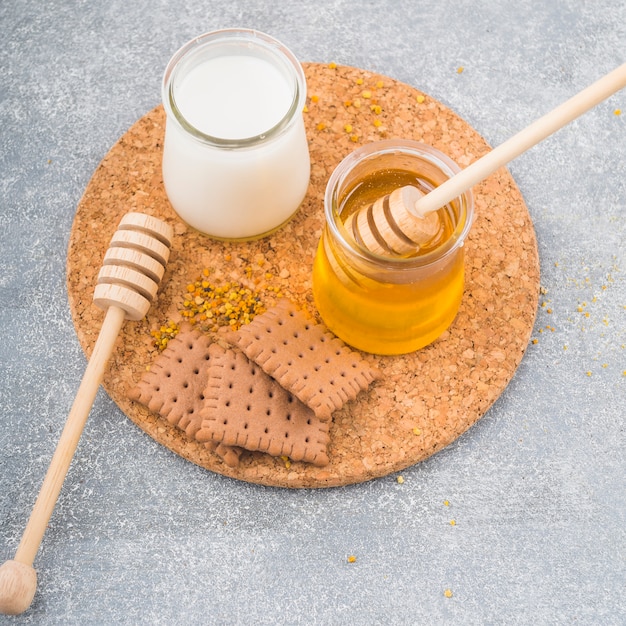 Milk and honey pot with baked biscuits on cork coaster