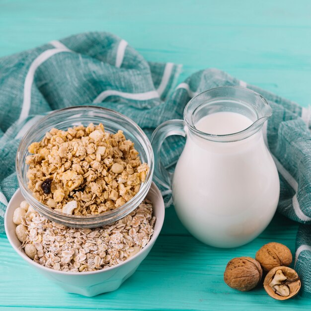 Milk jar; bowls of cereals and walnuts on green wooden table