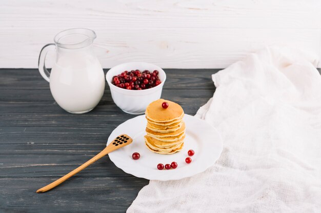 Milk jar; red currants berries and pancakes on wooden table