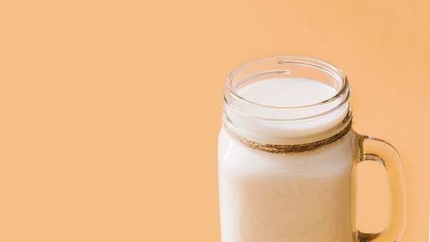 Milk in the opened glass jar over the colored background