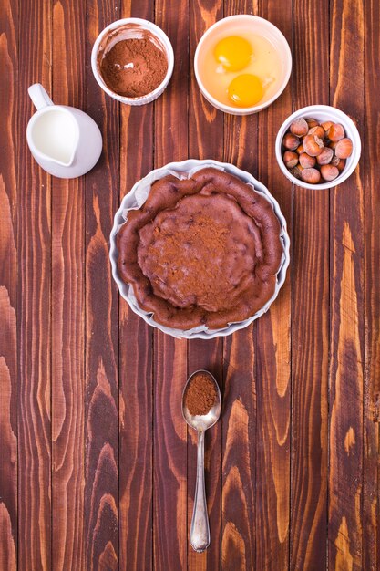 Milk pitcher; chocolate coffee powder; egg yolk and hazelnut for making fresh cake on wooden surface