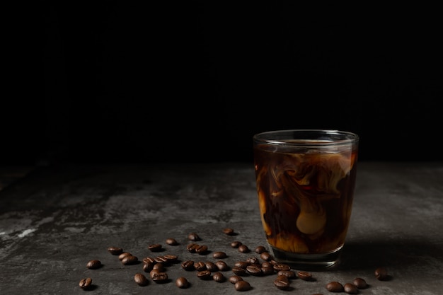 Milk pouring into iced black coffee on table