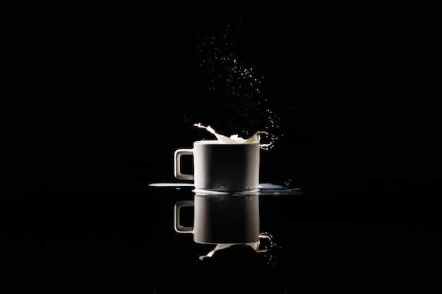 Free photo milk splashes in white cup on black background