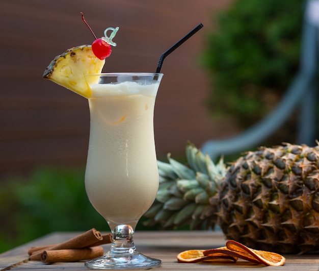 Milky cocktail in glass with pinapple slice and a cherry.
