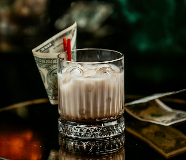 Free photo milky drink with ice cubes in whisky glass pinned with dollar