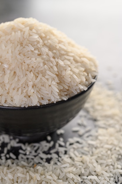 Milled rice in a black bowl on the black cement floor.