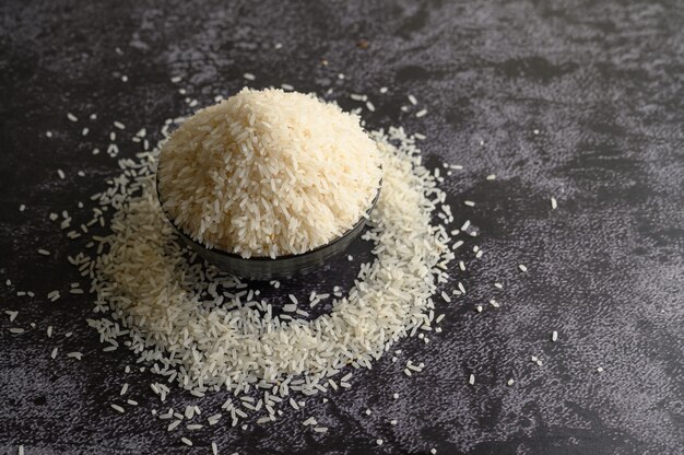 Milled rice in a black bowl on the black cement floor.