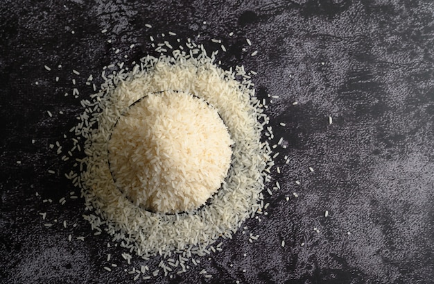 Milled rice in a black bowl on the black cement floor.