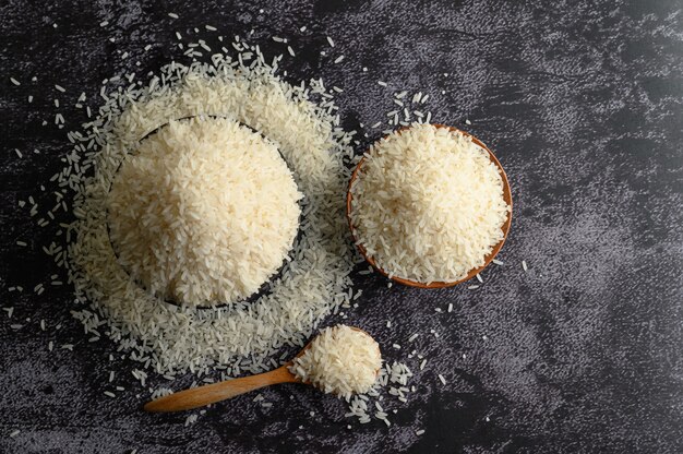 Milled rice in a bowl and a wooden spoon on the black cement floor.