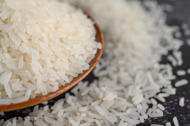 Milled rice in a bowl and a wooden spoon on the black cement floor.