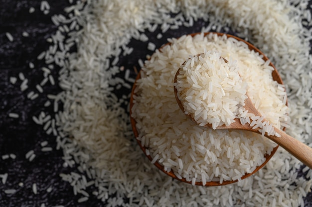 Milled rice in a bowl and a wooden spoon on the black cement floor.