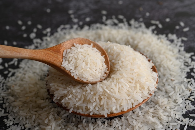 Milled rice in a bowl and a wooden spoon on the black cement floor.