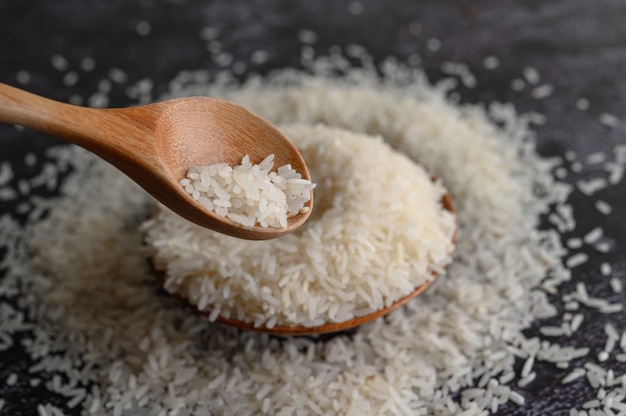 Milled rice in a bowl and a wooden spoon on the black cement floor.