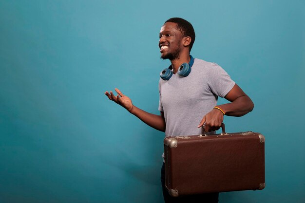 Millennial adult carrying voyage luggage in front of camera, feeling excited about tourist adventure with retro briefcase. Traveler preparing to leave on vacation journey with baggage.