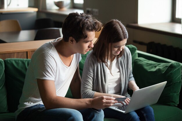 Millennial couple shopping online paying with credit card on laptop