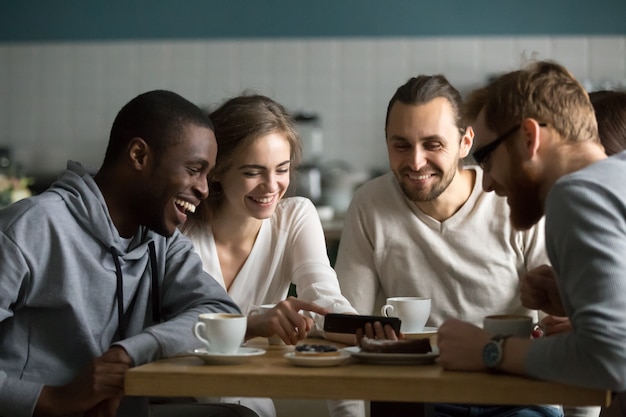 Millennial girl showing funny mobile video to friends in cafe