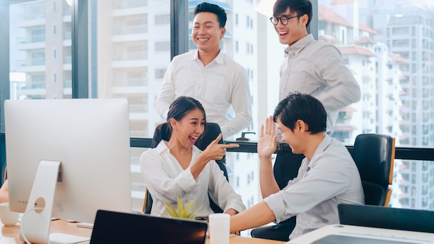 Millennial group of young businesspeople Asia businessman and businesswoman celebrate giving five after dealing feeling happy and signing contract or agreement at meeting room in small modern office.