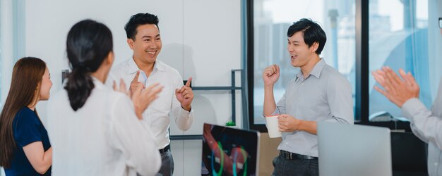 Millennial group of young businesspeople Asia businessman and businesswoman celebrate giving five after dealing feeling happy and signing contract or agreement at meeting room in small modern office.