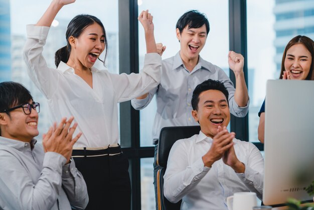 Millennial group of young businesspeople Asia businessman and businesswoman celebrate giving five after dealing feeling happy and signing contract or agreement at meeting room in small modern office.