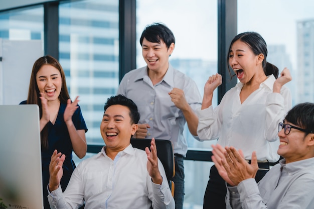 Millennial group of young businesspeople Asia businessman and businesswoman celebrate giving five after dealing feeling happy and signing contract or agreement at meeting room in small modern office.