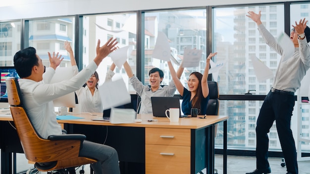 Millennial group of young businesspeople Asia businessman and businesswoman throwing documents feeling happy of achievements after succeed result at meeting room at small modern office in urban city.