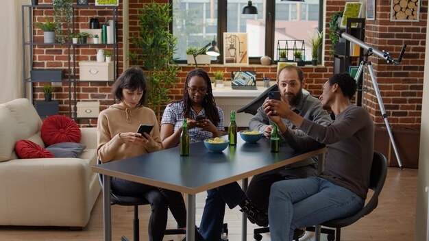 Millennial people hanging out together and browsing internet on smartphones, having fun with social media technology. Modern group of friends enjoying gathering with mobile phones.