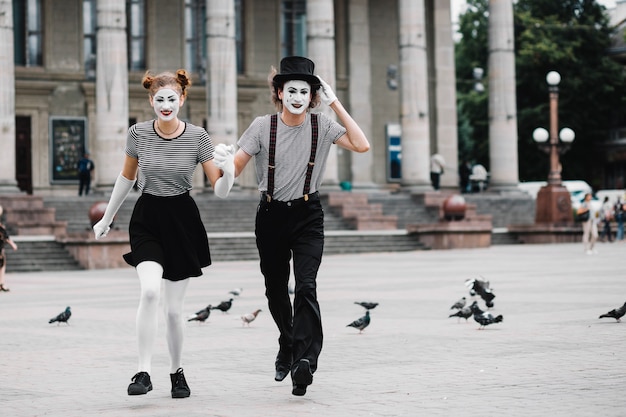 Mime couple running in front of building