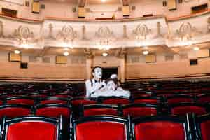 Free photo mime male artist playing with female mime's hair sitting together on chair in auditorium