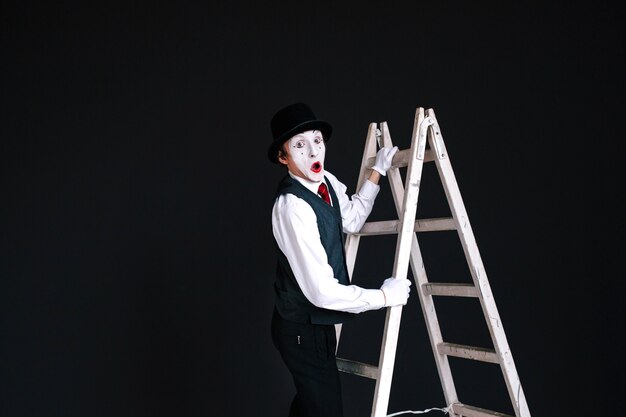 Mime stands on white ladder