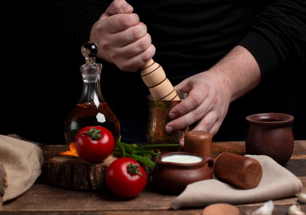 Mincing spices with wooden rolling pin on the table with vegetables