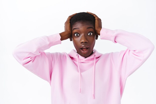 Mind-blowing news. Shocked african-american woman in pink hoodie grab head both arms and gasping