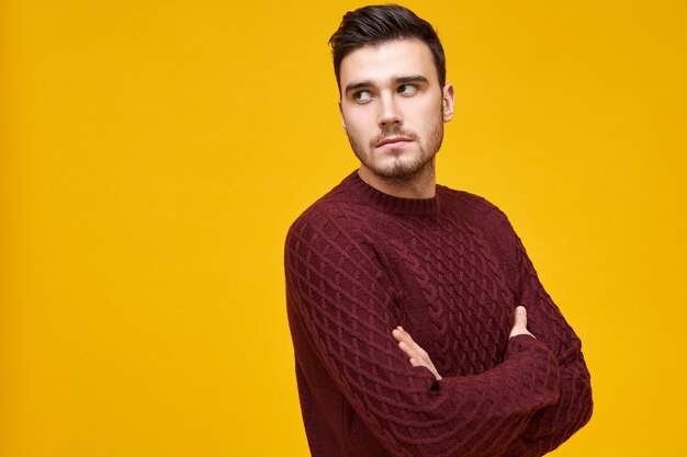 Mind your own business. Unhappy angry offended young unshaven male wearing warm knitted jumper posing isolated in closed posture, does not want to talk, ignoring you, feeling mad at his girlfriend