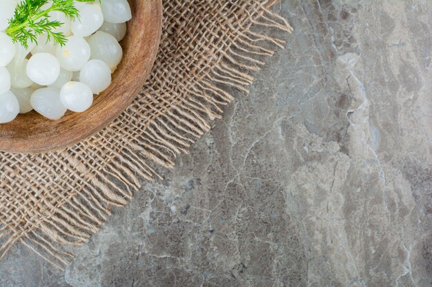 Mini baby onions on in a bowl on burlap napkin on marble.