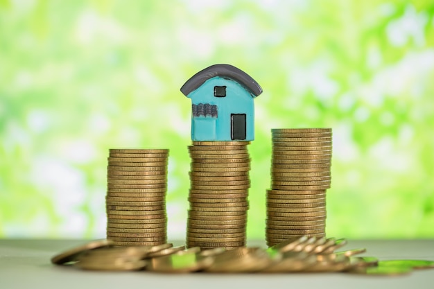 Mini house on stack of coins with green blur. 